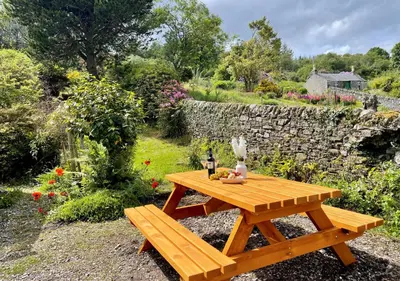 a wooden picnic table in a garden with a stone wall at Findhorn Upper Apartment in Kames
