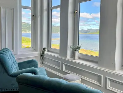 a living room with two blue chairs and windows at Findhorn Upper Apartment in Kames