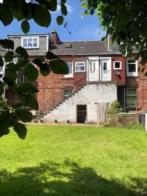 a house with a brick wall and a grass yard at Light & Spacious Loch Lomond Apartment in Alexandria