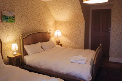a bedroom with two beds and two lamps and a door at Claggan Farmhouse, Loch Tay in Aberfeldy