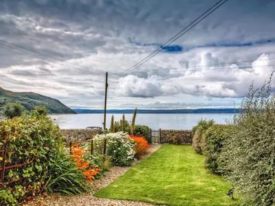 a garden with a pathway with flowers and a body of water at The Apostles in Catacol