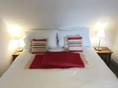 a white bed with two pillows and a red blanket on it at The Apostles in Catacol
