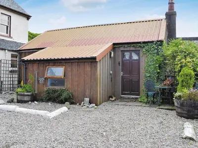 a wooden shed with a door in a yard at Port Righ Cottage in Carradale
