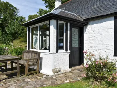 a white cottage with a bench and a table at Burnside Cottage in Sliddery