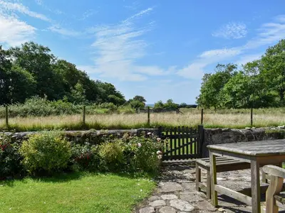 a picnic table in a garden with a fence and flowers at Burnside Cottage in Sliddery