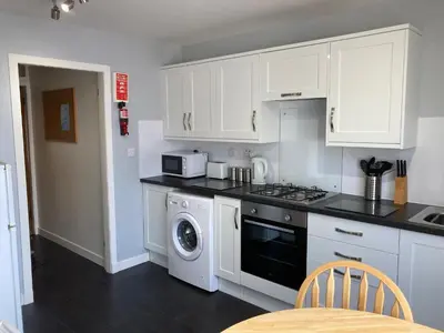a kitchen with white cabinets and a washer and dryer at Edgemont Annexe Oban in Oban