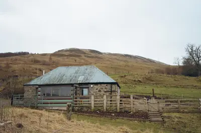 a small house in a field with a fence at Shepherds Forge, Loch Tay in Aberfeldy