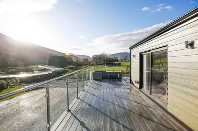a house with a deck with a view of a river at Castlehill cabin with a hot tub in Peebles