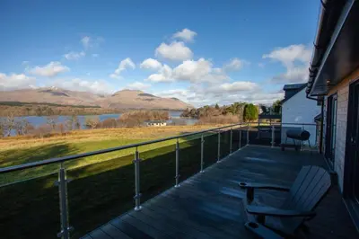a deck with a chair and a view of a lake at New Build Lodge With Stunning Views of Loch Awe in Hayfield