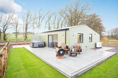 a tiny house with a deck and chairs in a yard at Shiphorns luxury cabin with a hot tub in Eddleston