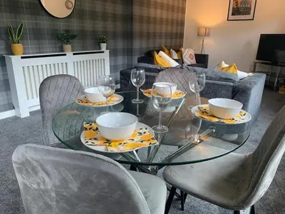 a glass table with chairs and glasses and a couch at Modern 2 bedroom flat with free parking in Cambuslang, Glasgow in Glasgow