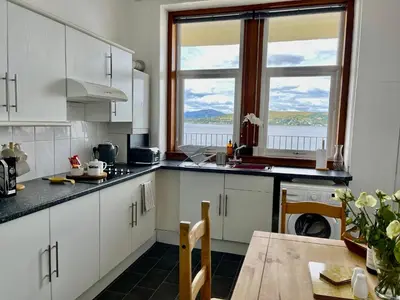 a kitchen with white cabinets and a table and two windows at A Shore Stay in Gourock