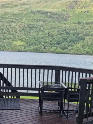a table and two chairs on a deck overlooking a lake at WATERSIDE 3 BED COTTAGE, HOT TUB, SAUNA, PVT BEACH in Arrochar