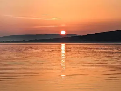 a sunset over a body of water with the sun setting at Strathclyde Cottage North in Skelmorlie