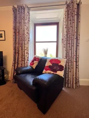 a black leather couch in a living room with a window at Beautiful Farm House at the foot of Ben More. in Crianlarich