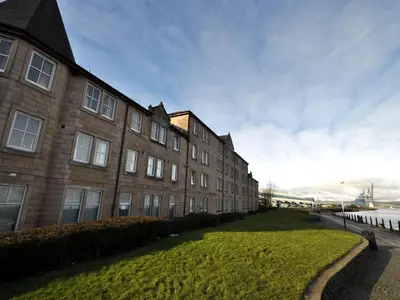 a building with a grass yard next to a body of water at The Waterfront in Greenock