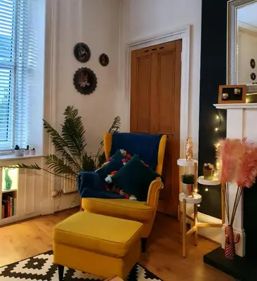 a living room with a yellow chair and a ottoman at The Flat with the Pink Door in Edinburgh
