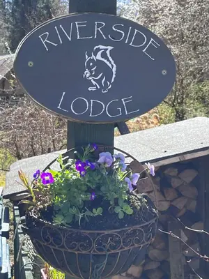a sign for the riverside lodge with a pot of flowers at Riverside Loft in Barcaldine