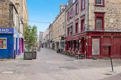 an empty street in a city with tables and chairs at JOIVY Modern Flat on Rose Street in Edinburgh