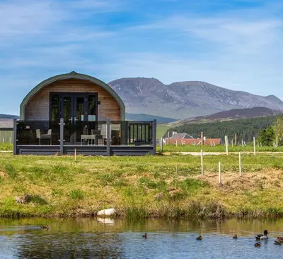 a small building with glass doors next to a body of water at Kings Caves Glamping in Torbeg