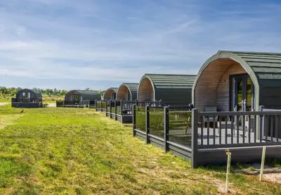 a row of green buildings with a fence in a field at Kings Caves Glamping in Torbeg