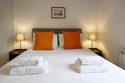a bedroom with a white bed with orange pillows and two lamps at George Street Apartment in Oban