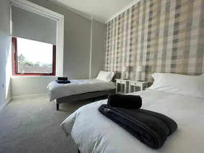 a white bedroom with two beds and a window at The Haven in Greenock
