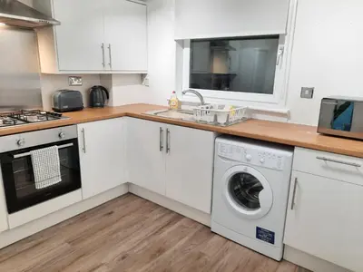 a kitchen with white cabinets and a washer and dryer at Ardfern Apartments in Airdrie