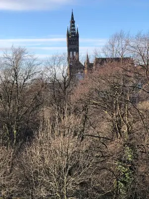 a clock tower in the distance behind some trees at The Kelvin - Peaceful West End River View Property in Glasgow