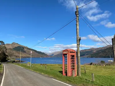 an old red phone booth on the side of a road at the waterside - carrick castle - loch goil in Carrick