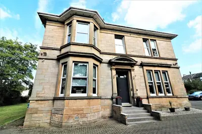 an old brick house with a black door at Signature - Linden House Flat 1 in Airdrie