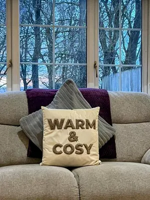 a pillow that says warm and cosy sitting on a couch at Hayloft at Bonnyside House in Bonnybridge