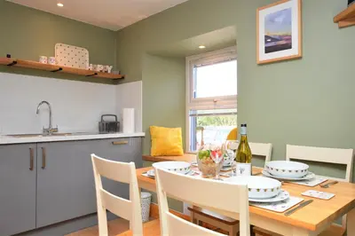 a kitchen and dining room with a wooden table and chairs at Chapelton Cottage in Strachur