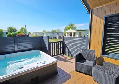 a hot tub on a deck with a chair at Heads Of Ayr Holiday Park in Ayr