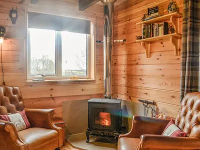 a living room with a fireplace and two chairs at Glenkens Lodge in Dalry