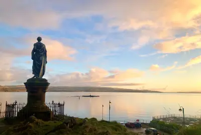 a statue of a man standing in front of a body of water at Glen Oirig in Hunters Quay
