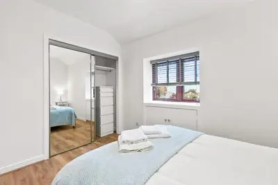 a white bedroom with a bed and a mirror at Aspen Apartment in Helensburgh