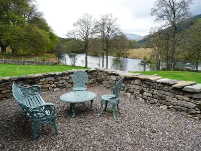 a table and two chairs sitting next to a stone wall at Riverside Cottage, Bridge of Balgie, Glenlyon, Perthshire in Bridge of Balgie