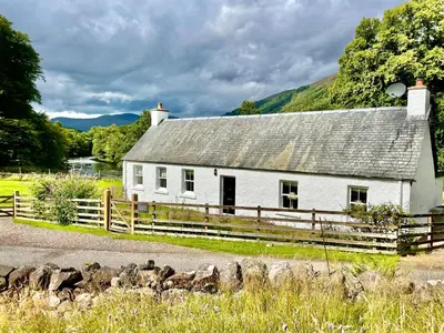 a white house with a fence in front of it at Riverside Cottage, Bridge of Balgie, Glenlyon, Perthshire in Bridge of Balgie
