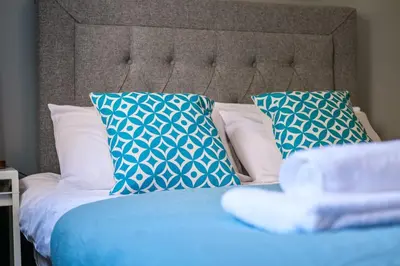 a bed with blue and white pillows on it at Monicas Apartment Lovely ground floor 2 bedroom serviced apartment in Coatbridge