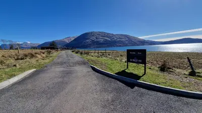 a road with a sign on the side of a lake at Dalrigh Pod in Onich