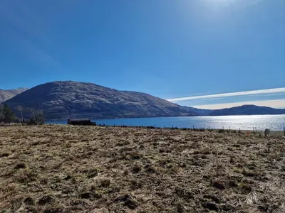 a field next to a body of water with a mountain at Dalrigh Pod in Onich