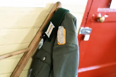 a green suit hanging on a wall next to a door at Cultybraggan Hut 37 in Comrie