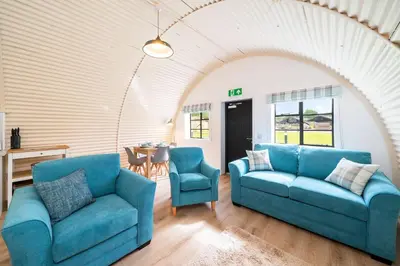a living room with two blue couches and a table at Cultybraggan Hut 35 in Comrie