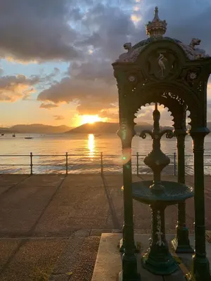 a clock on the beach with a sunset in the background at Lovely flat overlooking the Clyde in Gourock