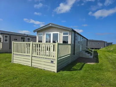 a small house with a fence in the grass at Machrihanish Holiday Park in Campbeltown