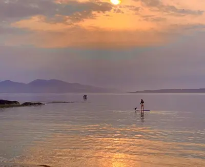 a man standing on a paddle board in the water at Linnhe Apartment, Kinlochlaich House in Appin