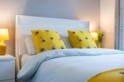 a bedroom with a white bed with yellow pillows at Lovely 3-bedroom flat with free parking in Bridge of Allan