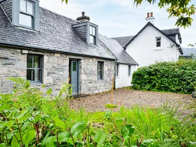 an old stone cottage with a garden in front of it at Oakwood Cottage - Glencoe in Glencoe
