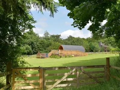 a wooden fence in front of a field with a barn at Pentland Pod - Cottage in Penicuik